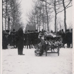 a coffin covered by flowers is surrounded by a group of mourners in black attire